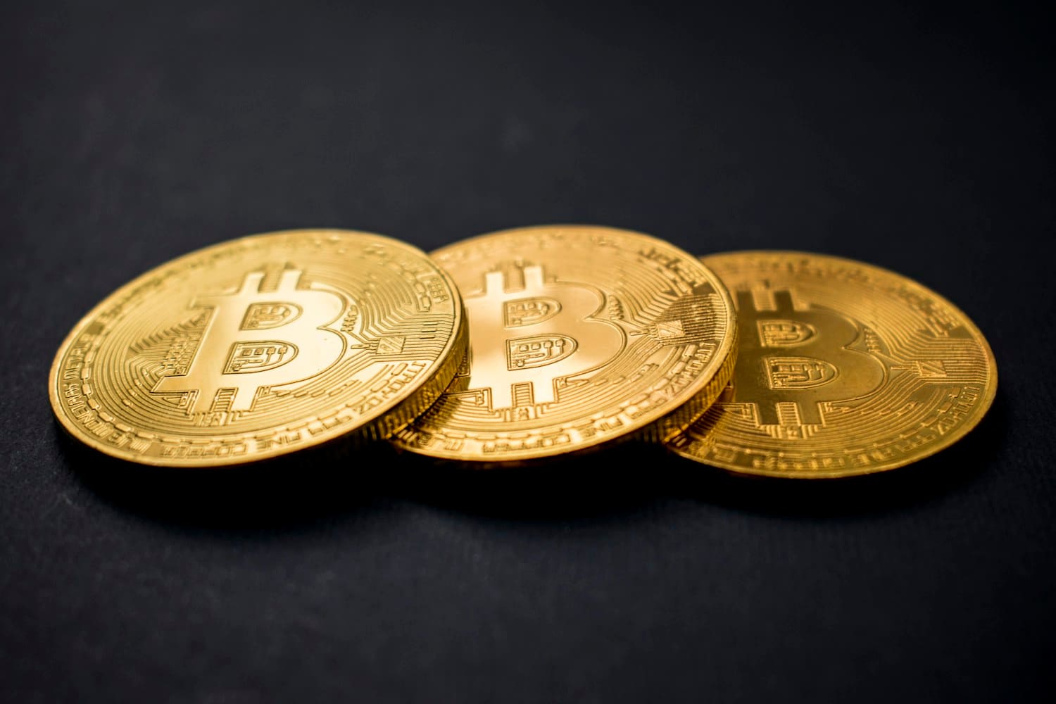 Gold Bitcoin coins on a dark reflective surface, representing digital assets traded on be1crypto.com